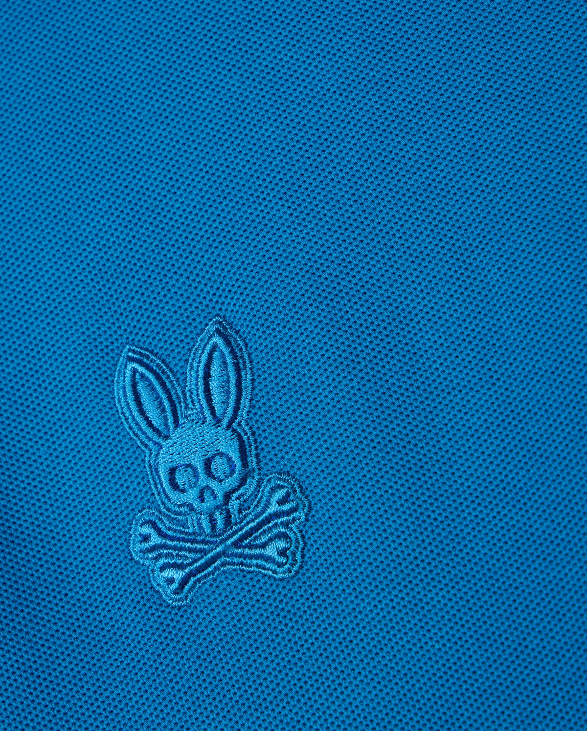 The blue BIG AND TALL MALTON PIQUE POLO SHIRT by Psycho Bunny features an embroidered rabbit skull and crossbones design with rabbit ears above crossed bones, set on a diamond pique pattern for added texture.