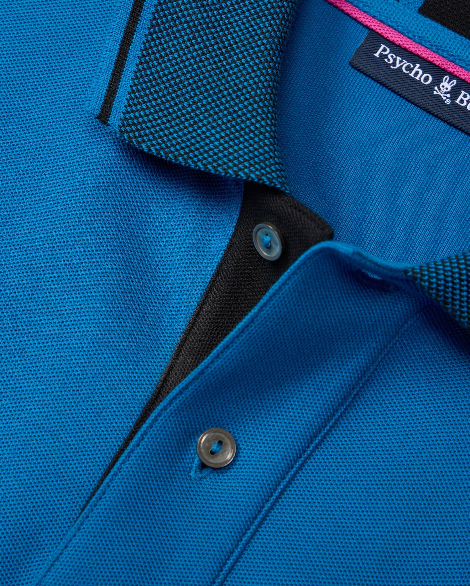 Close-up of a Psycho Bunny BIG AND TALL MALTON PIQUE POLO SHIRT - B9K950D200 in blue, featuring a textured collar with a black and blue diamond pique pattern, visible buttons on the placket, and an inside label showcasing its luxurious pima cotton craftsmanship.