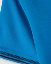 Close-up of a blue fabric in a diamond pique pattern with a folded corner, edged in checkered black and blue trim, reflecting the refined style of the Big and Tall Malton Pique Polo Shirt by Psycho Bunny.