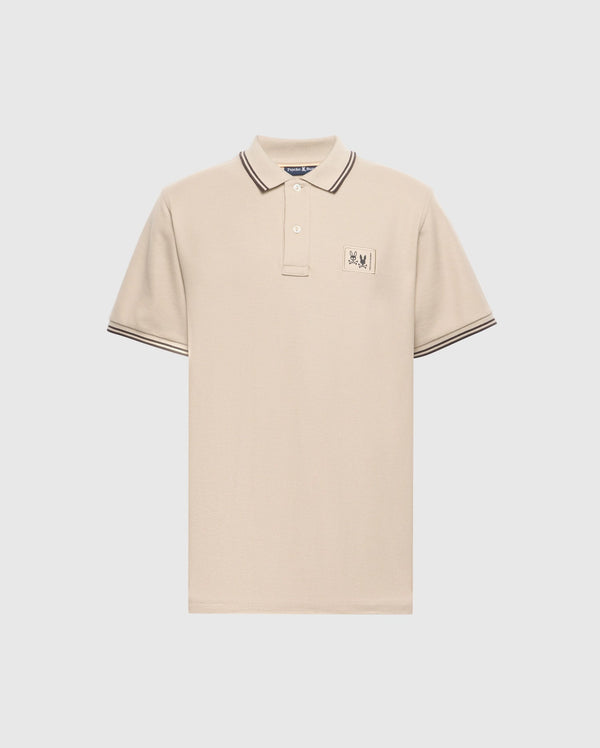 The Psycho Bunny Men's Big and Tall Monroe Pique Polo - B9K964D200 is a regular-fit, beige polo made from Pima cotton, featuring a buttoned collar with black stripes on the edges, short sleeves with striped cuffs, and an embroidered chest emblem.