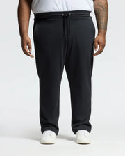 Someone in comfortable black Psycho Bunny BIG AND TALL ALEXANDER SWEATPANT - B9P155E200 and white sneakers stands against a white background. The joggers have a drawstring elastic waistband, and the person's left arm displays a tattoo.
