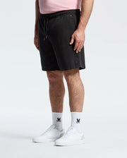 A person in a pink, regular-fit shirt and Psycho Bunny black shorts stands with hands by their sides. Their white socks feature a black logo with a subtle bunny pattern, paired perfectly with white sneakers against a plain white background.