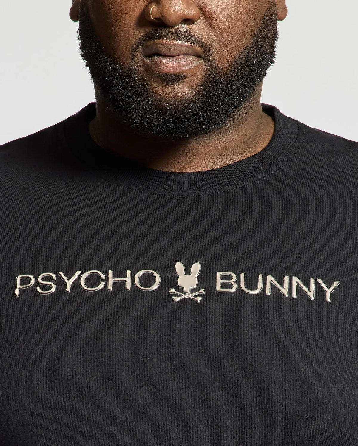 A person wears a black "Psycho Bunny" shirt with a small bunny and crossbones logo, showcasing the premium quality of the BIG AND TALL LAVATA FRENCH TERRY SWEATSHIRT - B9S159E200. The chest-up view highlights its luxurious French Terry feel.