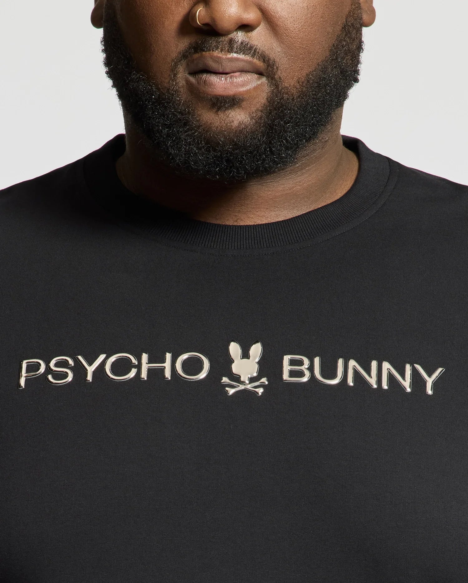 A person wears a black "Psycho Bunny" shirt with a small bunny and crossbones logo, showcasing the premium quality of the BIG AND TALL LAVATA FRENCH TERRY SWEATSHIRT - B9S159E200. The chest-up view highlights its luxurious French Terry feel.