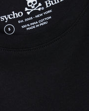 A close-up of the Psycho Bunny men's Big and Tall Classic Crew Neck Tee (B9U014CRPC) reveals a black T-shirt with white text inside featuring a skull and crossbones, the word "Psycho," "100% Pima Cotton," "Made in Peru," "Est. 2005 - New York," and size label "5.