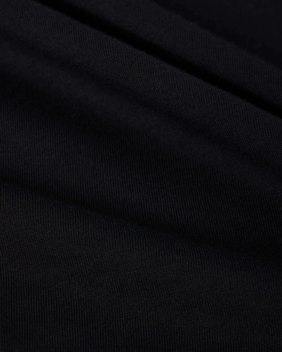 A close-up of black, finely ribbed fabric with subtle folds from the Psycho Bunny MENS BIG AND TALL CLASSIC CREW NECK TEE (B9U014CRPC) reveals a textured appearance. Lighting highlights its ridges and grooves, indicating it is soft and flexible 100% Pima cotton.