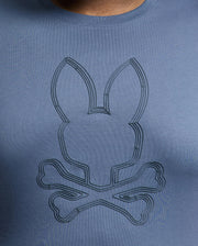 The MENS BIG AND TALL MONARC FRONT BUNNY GRAPHIC TEE by Psycho Bunny is crafted from soft Pima cotton. This blue tee features a stylized rabbit head above crossed bones in a subtly darker shade, showcasing Monarc's unique design flair.