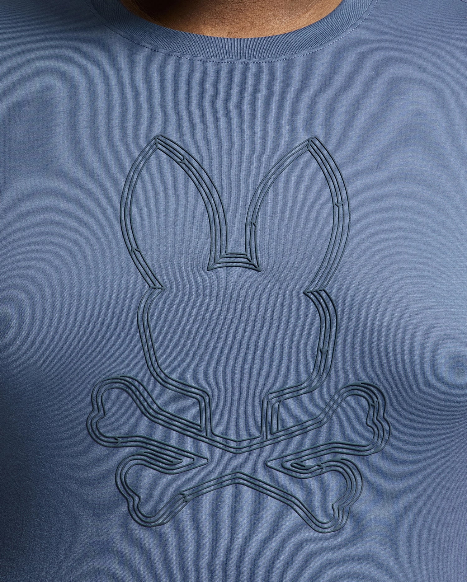 The MENS BIG AND TALL MONARC FRONT BUNNY GRAPHIC TEE by Psycho Bunny is crafted from soft Pima cotton. This blue tee features a stylized rabbit head above crossed bones in a subtly darker shade, showcasing Monarc's unique design flair.