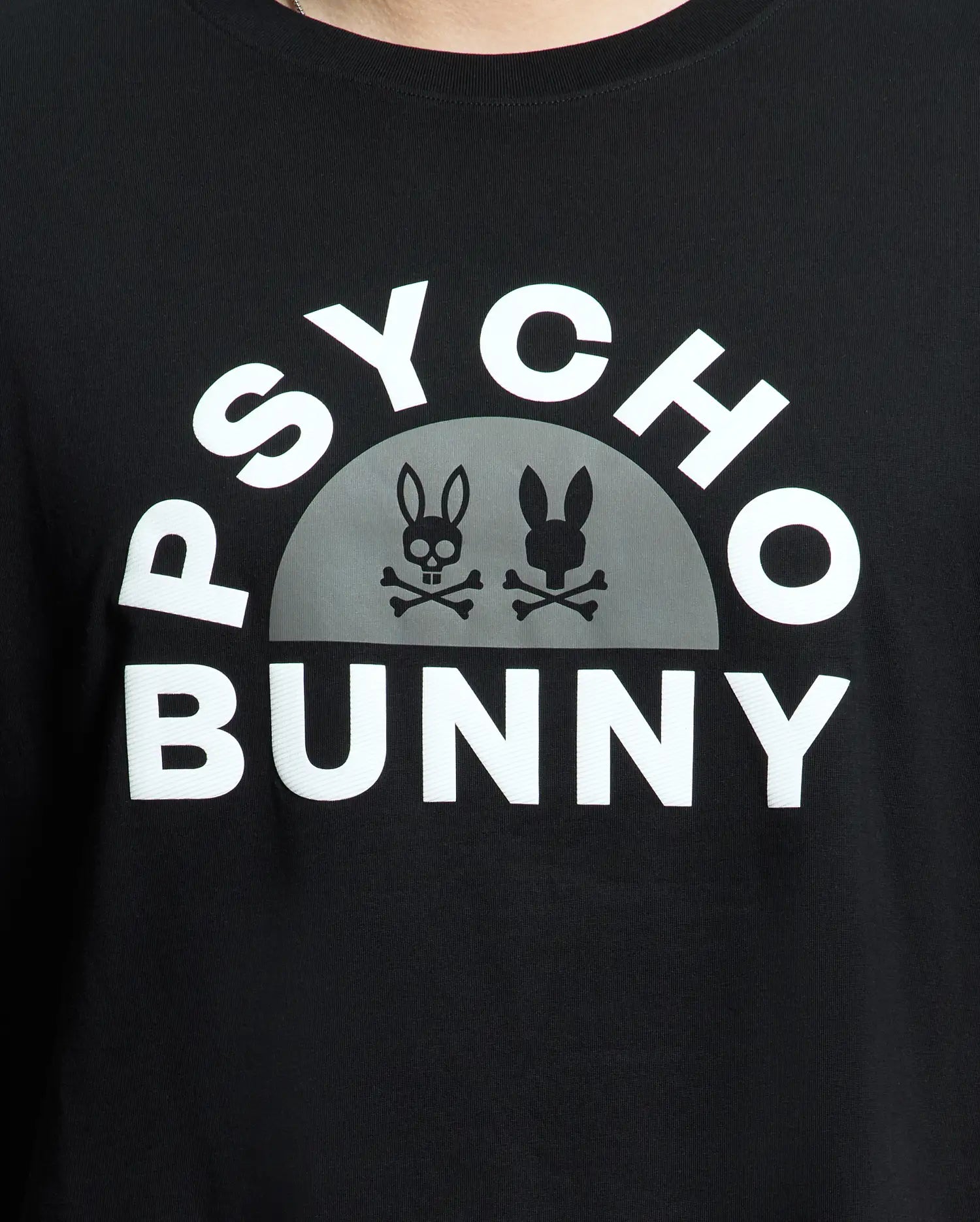 The Men's Big and Tall Goldie Graphic Tee from Psycho Bunny features "Psycho Bunny" in white on premium Pima cotton. Below it, a semicircle displays two bunny skull logos with crossbones, one light and one dark, highlighting the edgy graphic style.