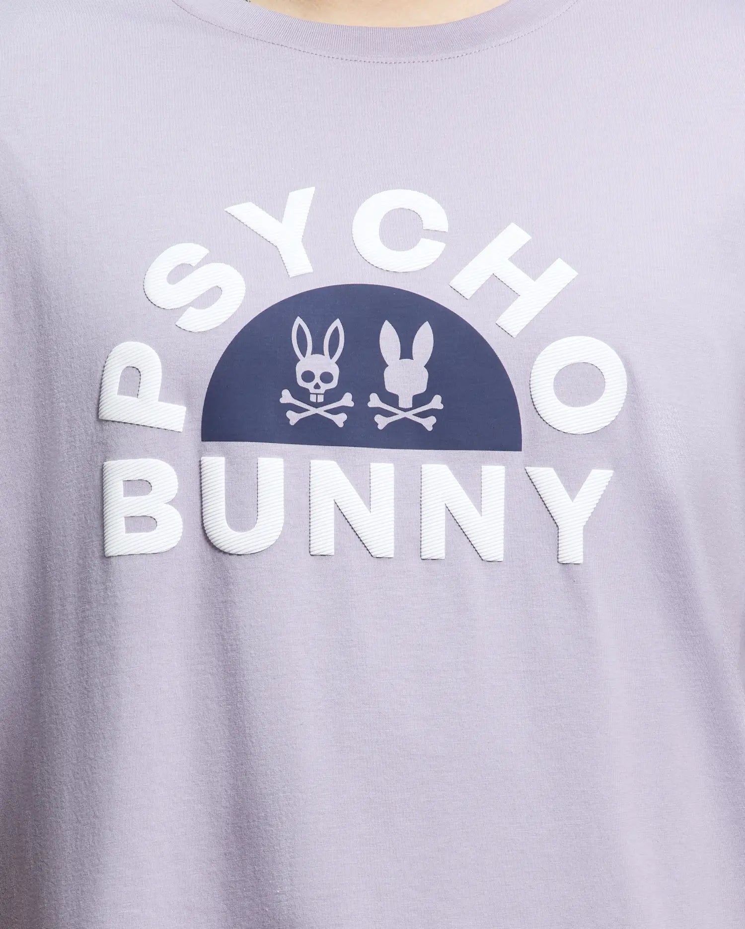 Close-up of the Men's Big and Tall Goldie Graphic Tee (B9U606F200) by Psycho Bunny in light purple, crafted from soft Pima cotton. It showcases bold white "Psycho Bunny" text with a dark arch and bunny graphic icons, one resembling a skull and crossbones.