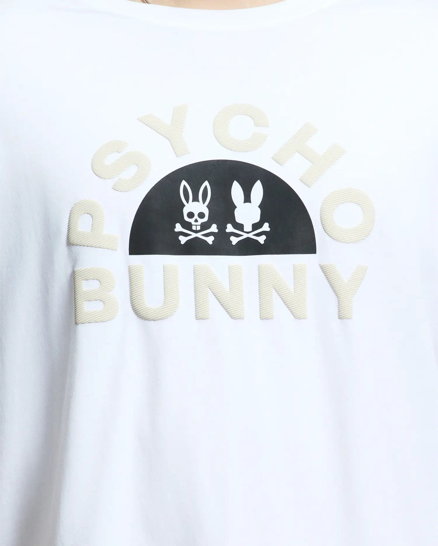 Close-up of a MENS BIG AND TALL GOLDIE GRAPHIC TEE - B9U606F200 by Psycho Bunny, crafted from Peruvian Pima cotton. It features "Psycho Bunny" in beige letters with a black half-circle displaying a white skull-and-crossbones within the bunny graphic.