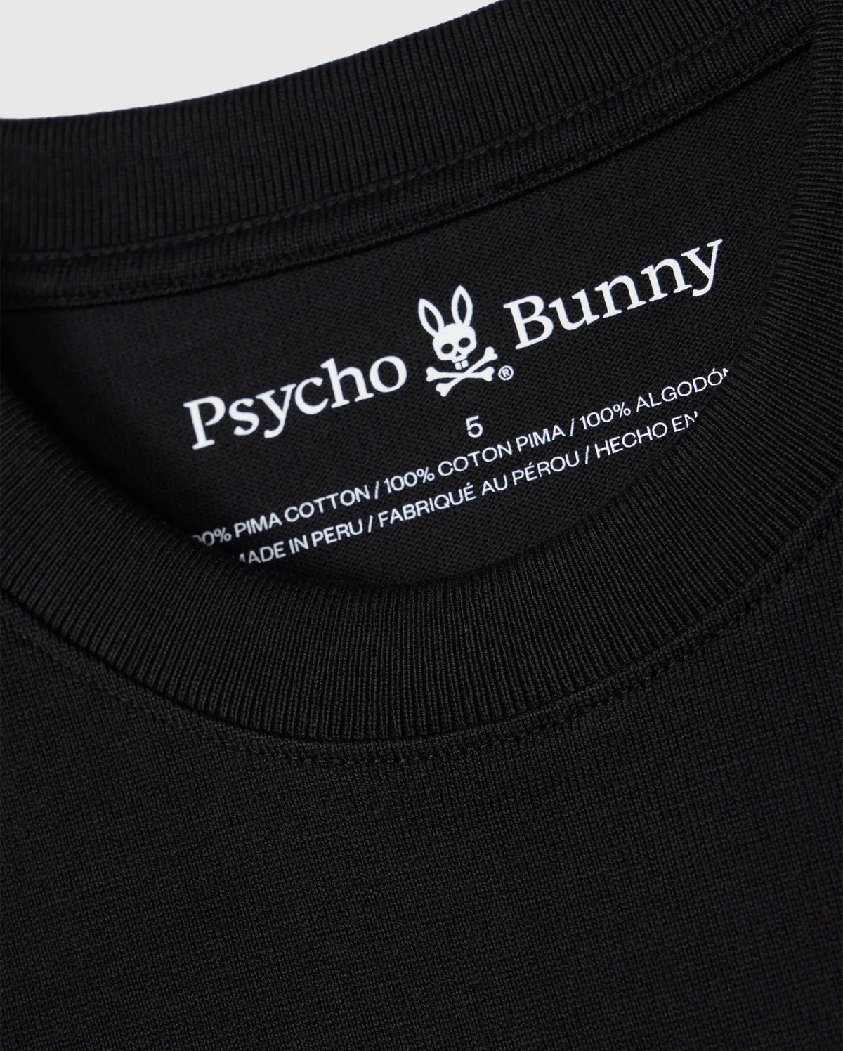 Close-up of the label on a black Psycho Bunny BIG AND TALL DUKE OVERSIZED TEE - B9U742D200, displaying the brand name with a rabbit skull logo. Made from heavyweight 100% Pima cotton and "Made in Peru," showcasing the quality of this relaxed-fit shirt.