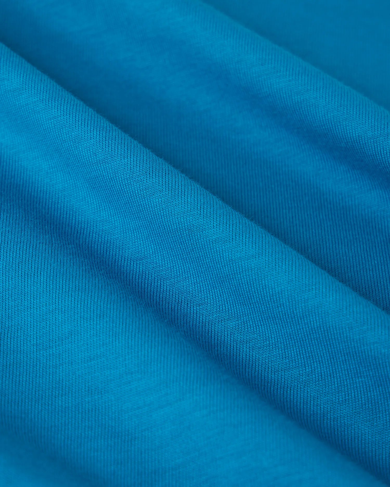 Close-up of the vibrant blue Pima cotton used in the Psycho Bunny BIG AND TALL MALTON GRAPHIC TEE - B9U795D200, featuring fine diagonal lines for a textured look. The soft fabric showcases Peruvian craftsmanship with gentle folds suggesting movement and fluidity.