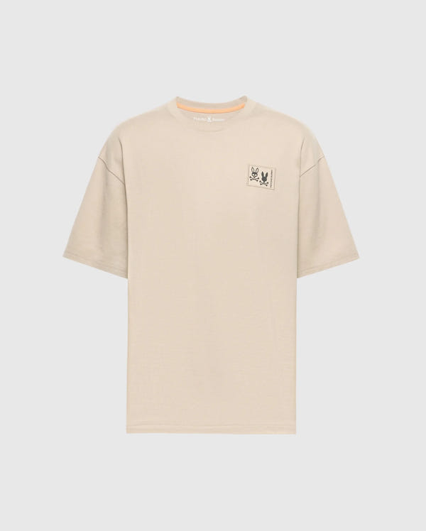 The Psycho Bunny Men's Big and Tall Monroe Oversized Tee - B9U910D200 is a light beige, soft pima cotton T-shirt with a relaxed fit crew neckline, short sleeves, and a minimalistic rectangle graphic with an illustration and text on the left chest against a white background.