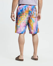 A person is shown from behind wearing a short-sleeved gray shirt, Psycho Bunny Big and Tall Milos Swim Trunk with a colorful abstract pattern of pink, blue, orange, and yellow in quick-dry fabric, and brown sandals.