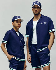 A man and child, both in Psycho Bunny MENS BASIL TAPED SHORT - MB0900005 and matching shirts in navy, with elastic waists and crafted from a cotton-modal blend, stand confidently against a neutral background.