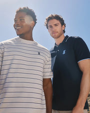 A model wearing the mens pima cotton alton stripe heavy weight tee standing next to another model wearing the Men's Houston pique polo shirt in navy outside in the sunshine