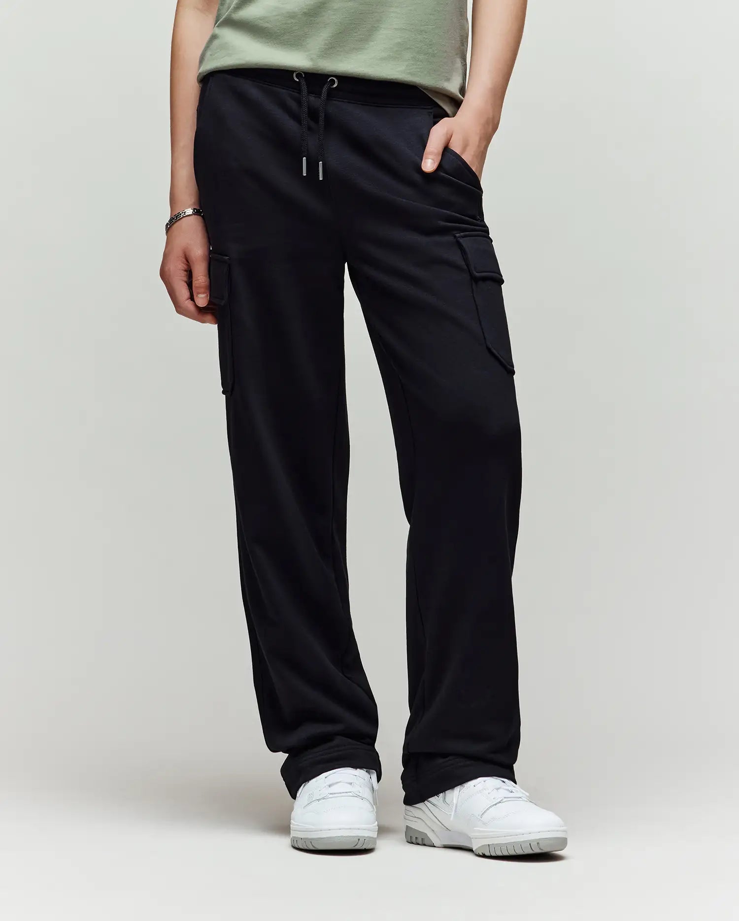 A child models Psycho Bunny’s KIDS NASH CARGO SWEATPANT - KB0800004 in green, showcasing utility cargo pockets and sweatpant comfort, with only the lower half and white sneakers visible against a plain light background.