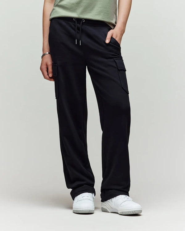 A child models Psycho Bunny’s KIDS NASH CARGO SWEATPANT - KB0800004 in green, showcasing utility cargo pockets and sweatpant comfort, with only the lower half and white sneakers visible against a plain light background.