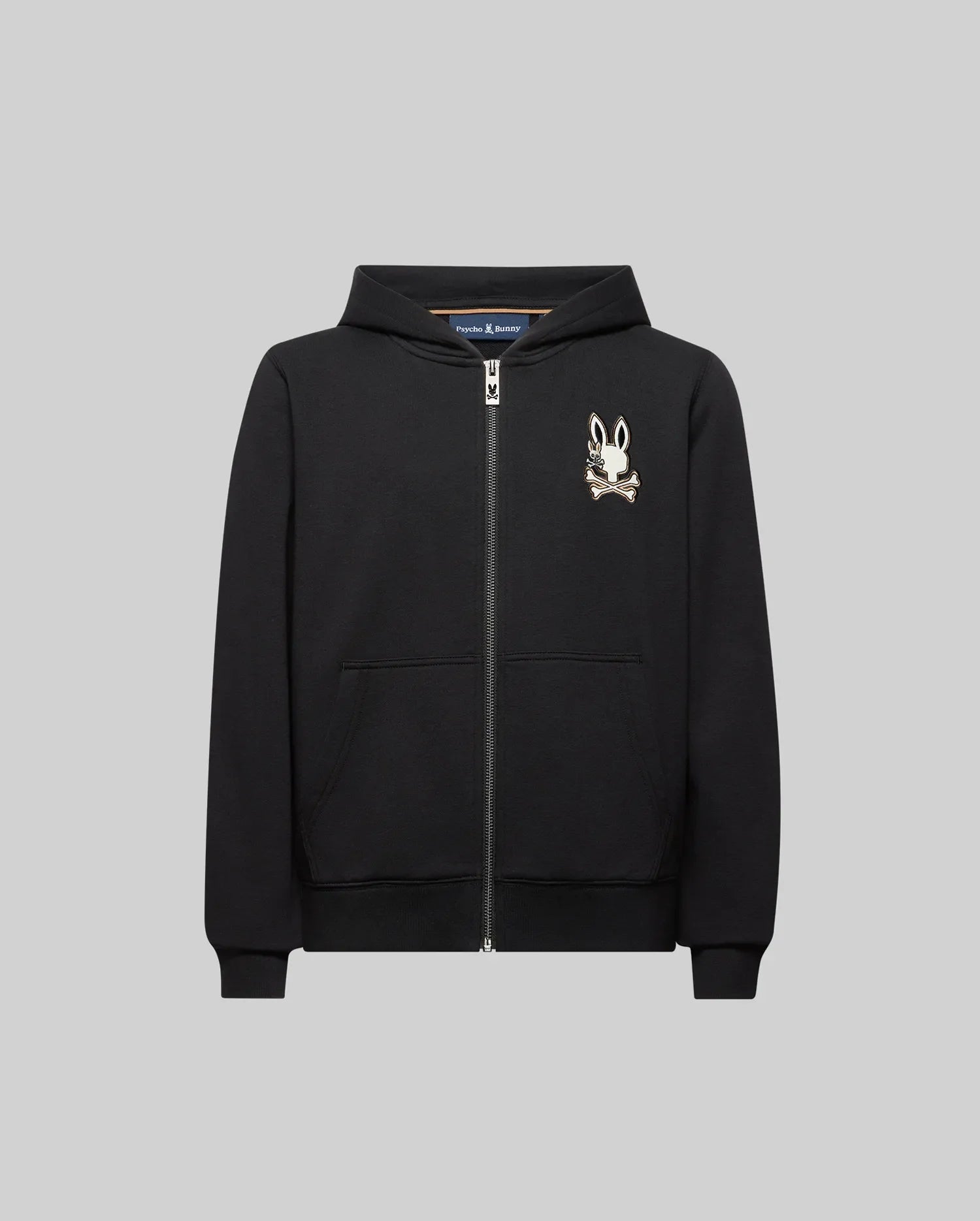 The KIDS WADE CORD PATCH ZIP HOODIE (KT0500016) by Psycho Bunny is a black zip-hoodie with front pockets, crafted from premium cotton, and features an embroidered Bunny head with crossbones on the left chest.
