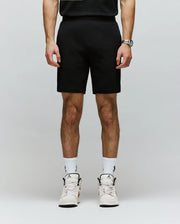 A person, shown from the shoulders down, wears Psycho Bunny MENS LAZSLO SWEATSHORT - MB0900016 in a stretch modal-cotton blend, paired with a black shirt, wristwatch, white logo socks, and white sneakers for an effortless casual look.