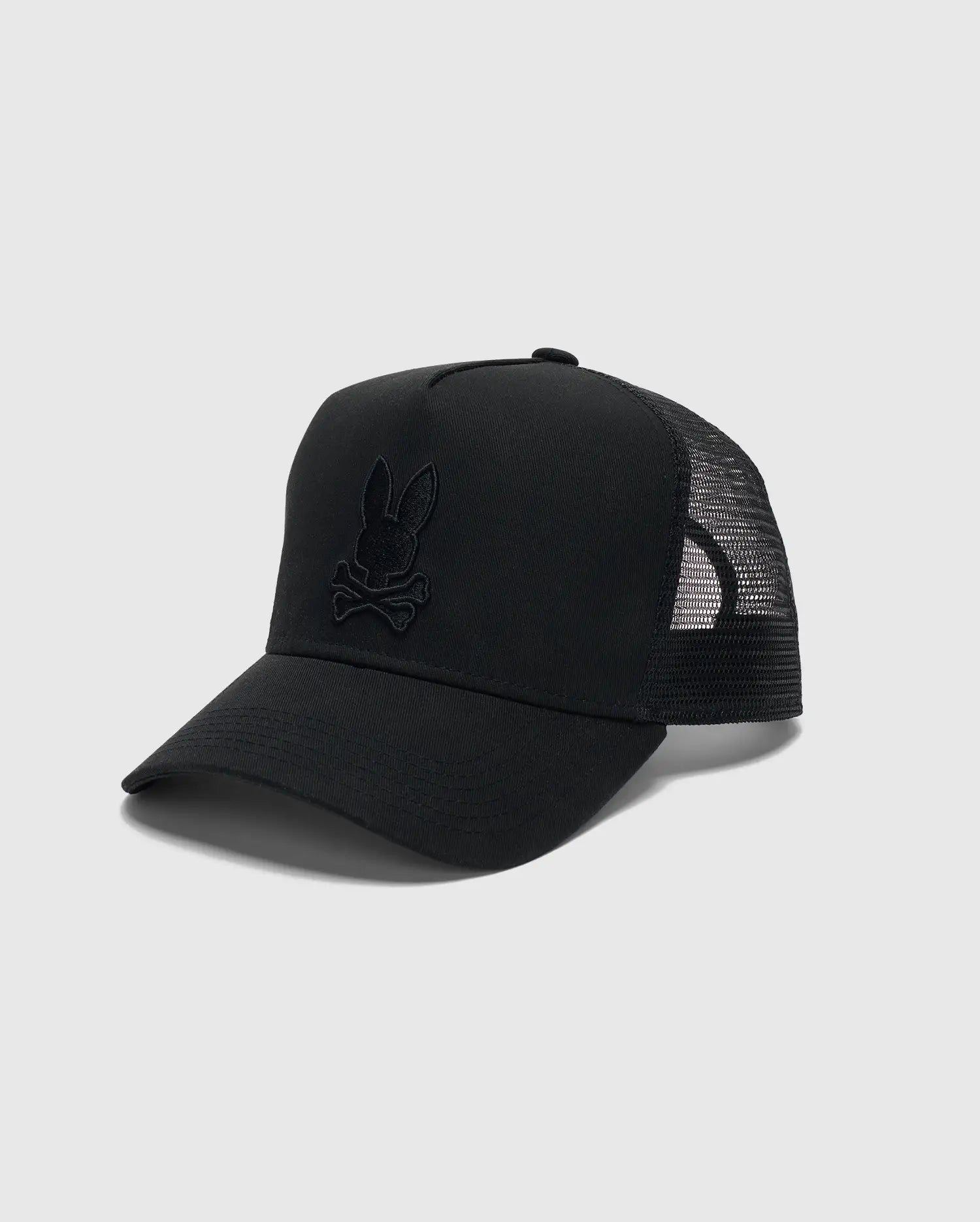 The Psycho Bunny Men's Wilder Trucker Cap (MO1500026) features a black colorway with a curved brim and mesh back. An embroidered rabbit head with crossed bones stands out on a light gray front panel, complete with an adjustable strap for the ultimate rugged style fit.