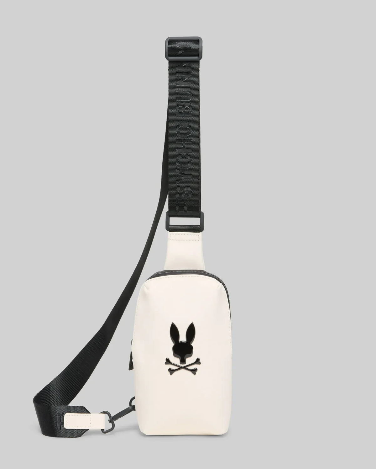 Mens Rubberized Crossbody in cream, featuring a smooth finish, a prominent black Psycho Bunny skull logo on the front, and an adjustable black strap with repeated brand text.