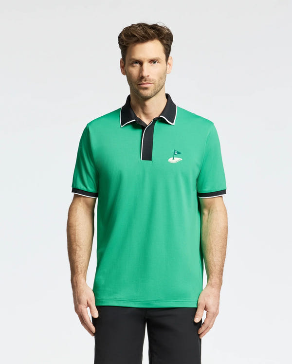 A man stands against a plain white background, showcasing the Psycho Bunny MENS CLAYTON PIQUE POLO - MT0100004. Made from premium Pima cotton, this breathable polo features a small golf hole and flag logo on the chest and has contrasting black collar and sleeve trim.