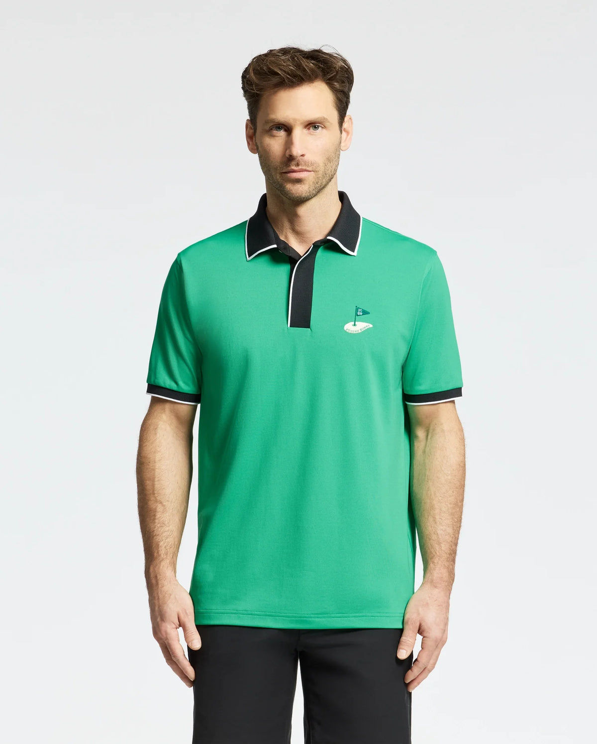 A man stands against a plain white background, showcasing the Psycho Bunny MENS CLAYTON PIQUE POLO - MT0100004. Made from premium Pima cotton, this breathable polo features a small golf hole and flag logo on the chest and has contrasting black collar and sleeve trim.