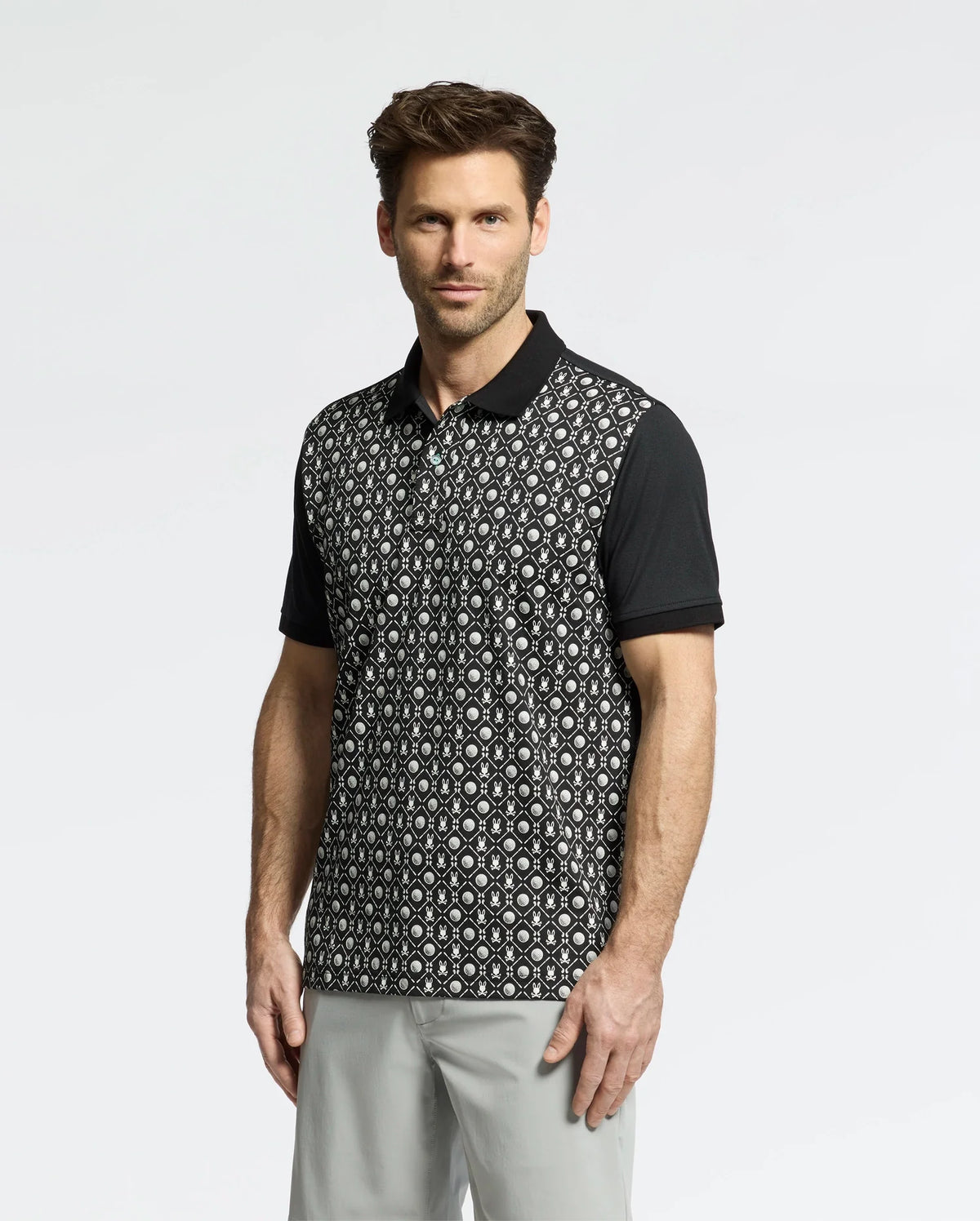 A man is wearing a Psycho Bunny MENS BECKETT PIQUE POLO - MT0100022 with black sleeves and collar, paired with light gray pants, against a light background.