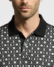A man is wearing the Psycho Bunny MENS BECKETT PIQUE POLO (MT0100022), made of breathable black Pima cotton with white cartoon bunny faces and circular shapes. Facing the camera, he showcases its distinctive black collar and upper body design.