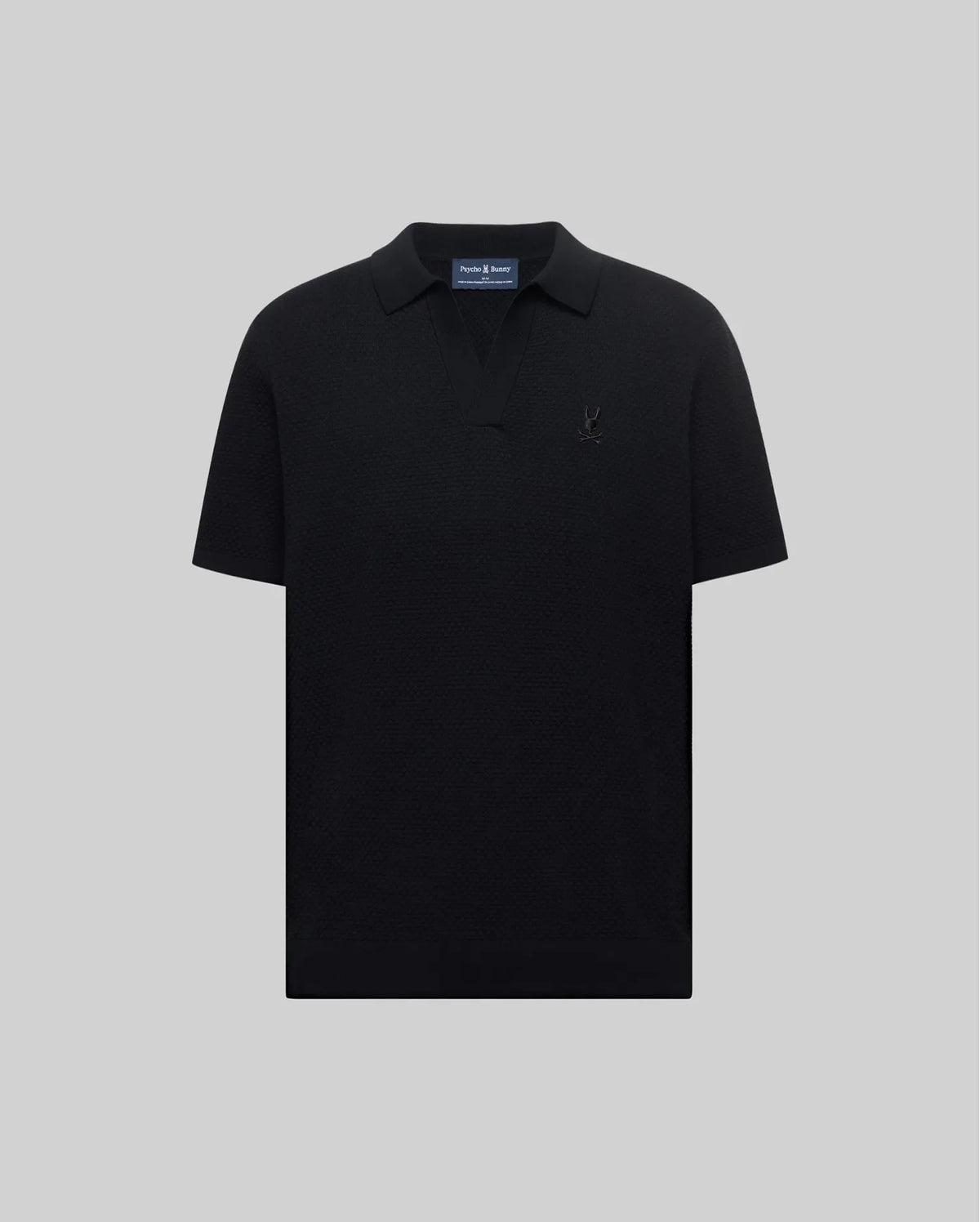 Mens Devon Knit Polo in black, featuring a subtle textured knit, classic fit, V-neck placket, and a tonal embroidered Psycho Bunny skull logo on the left chest.
