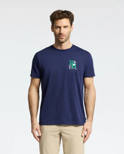 A man with short brown hair wears the navy blue Psycho Bunny MENS DENIS GRAPHIC TEE - MT0200015, made from soft Pima cotton with a small embroidered logo on the upper left. He pairs it with beige pants for a golf-inspired look, standing against a plain white background.