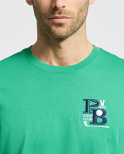 A man dons the Psycho Bunny MENS DENIS GRAPHIC TEE - MT0200015 in green Pima cotton, showcasing an embroidered "PB" and "GOLF CLUB" in blue and white on the chest for a golf-inspired style against a plain white backdrop.