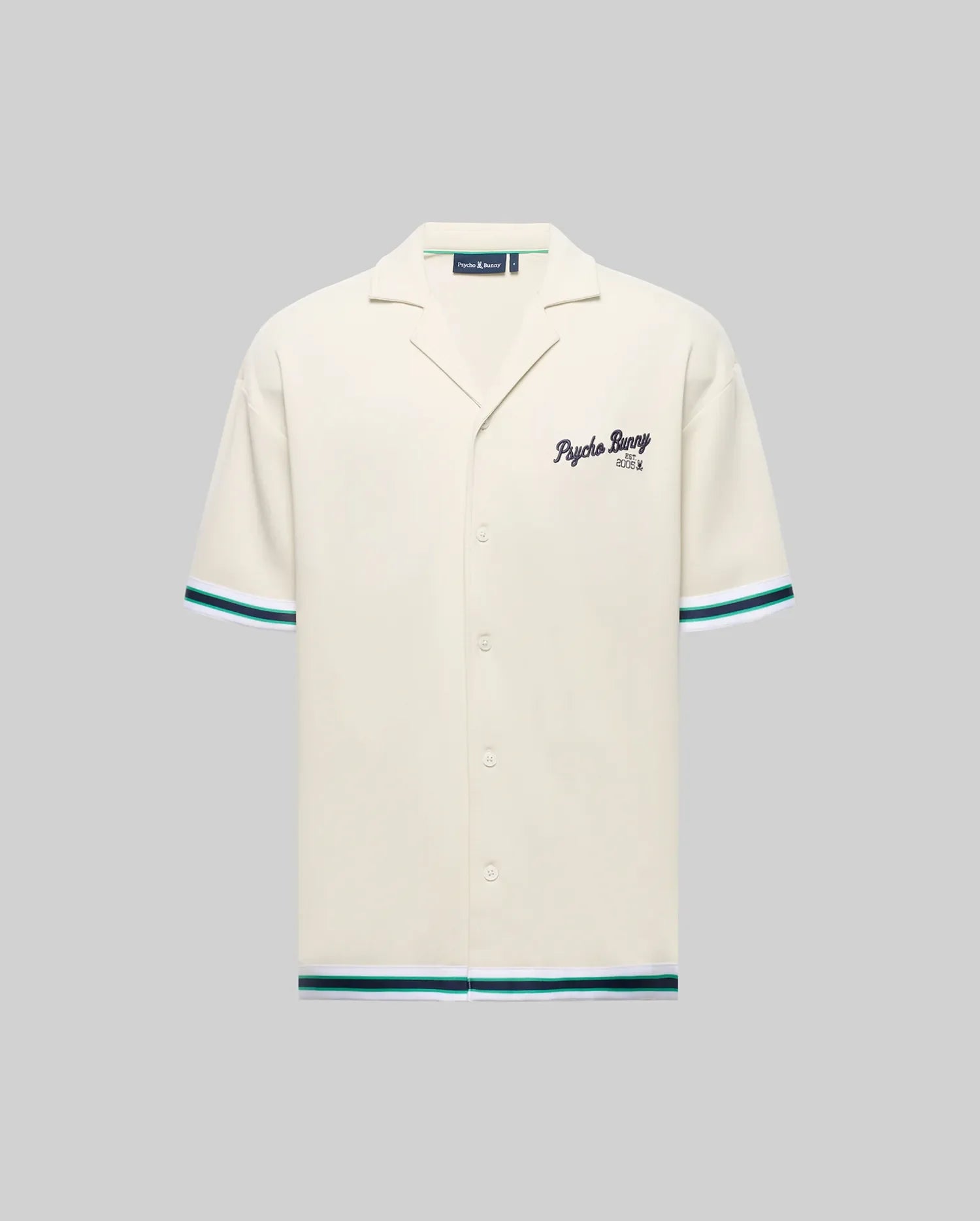 The Psycho Bunny MENS BASIL TAPED CAMP COLLAR SHIRT (MT0500004) is cream-colored, made of a cotton-modal blend with short sleeves, green/blue stripe accents, a Johnny collar, and embroidered "Psycho Bunny" text on the left chest.