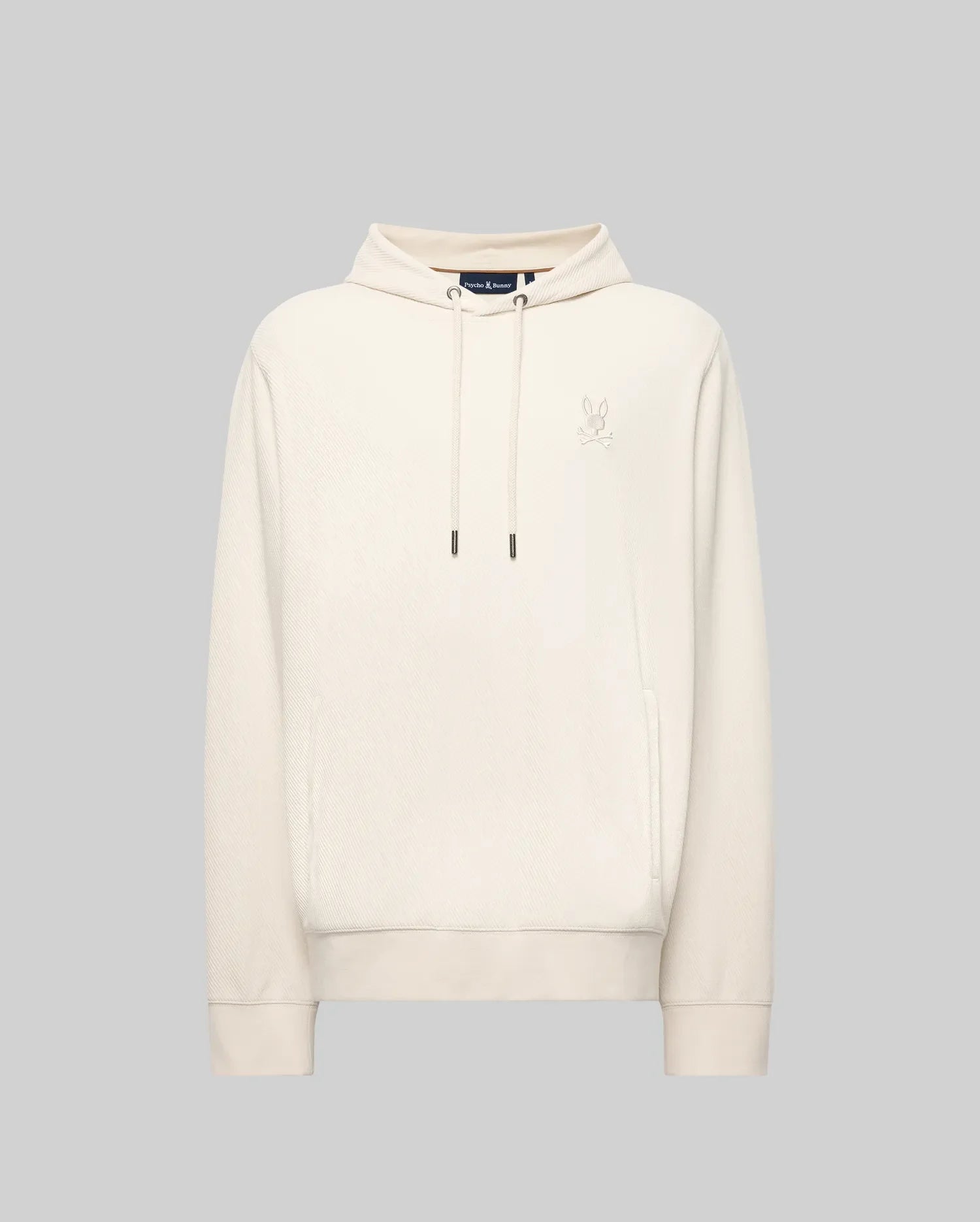 The Psycho Bunny MENS KAI HOODIE - MT0500019 is a plain light beige hoodie with long sleeves, a front pocket, and a small embroidered Bunny logo on the left chest, shown against a solid light grey background.