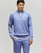 A man wears the Psycho Bunny MENS SHAWN QUARTER ZIP SWEATSHIRT - MT0500115 in light purple with matching shorts, both featuring a small bunny logo, standing against a plain background and looking at the camera with one hand in his pocket.