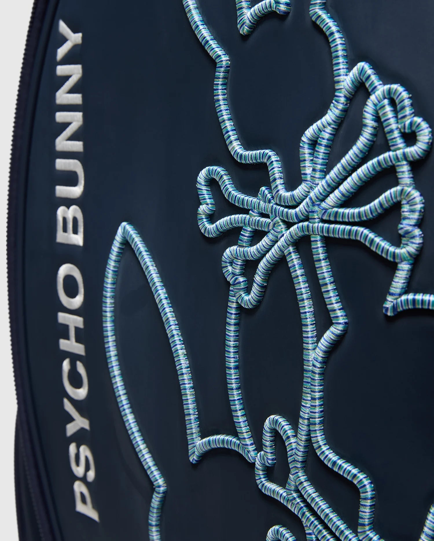 Close-up of the OUTLINE BUNNY GOLF TOUR BAG - PBMG4FC1 by Psycho Bunny, showcasing "Psycho Bunny" in white on the left, with a stylized outlined bunny using turquoise stitching on dark fabric. Made from durable polyurethane, it includes a detachable strap for versatile carrying.