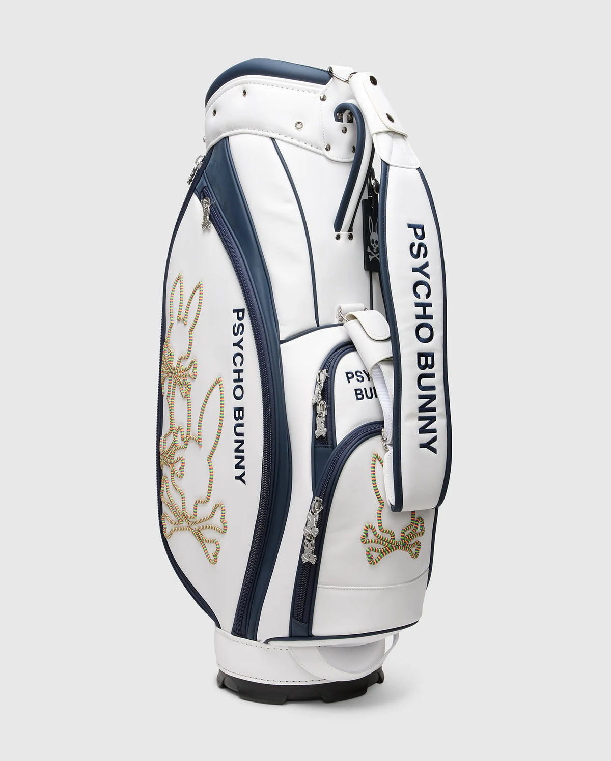 The OUTLINE BUNNY GOLF TOUR BAG - PBMG4FC1 by Psycho Bunny is a white and navy polyurethane cart bag adorned with gold embroidered bunny designs. It includes five-pocket club dividers and multiple zippered compartments, merging sporty style with functionality for golfers.