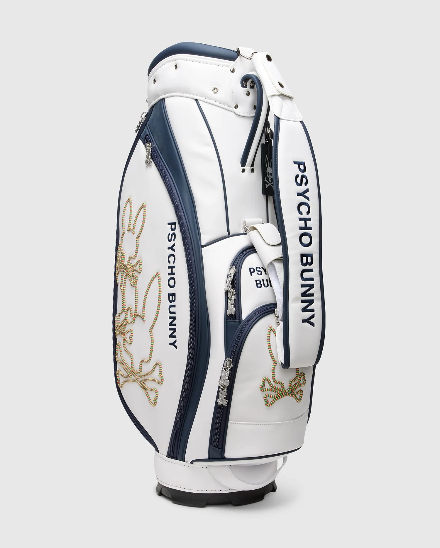 The OUTLINE BUNNY GOLF TOUR BAG - PBMG4FC1 by Psycho Bunny is a white and navy polyurethane cart bag adorned with gold embroidered bunny designs. It includes five-pocket club dividers and multiple zippered compartments, merging sporty style with functionality for golfers.