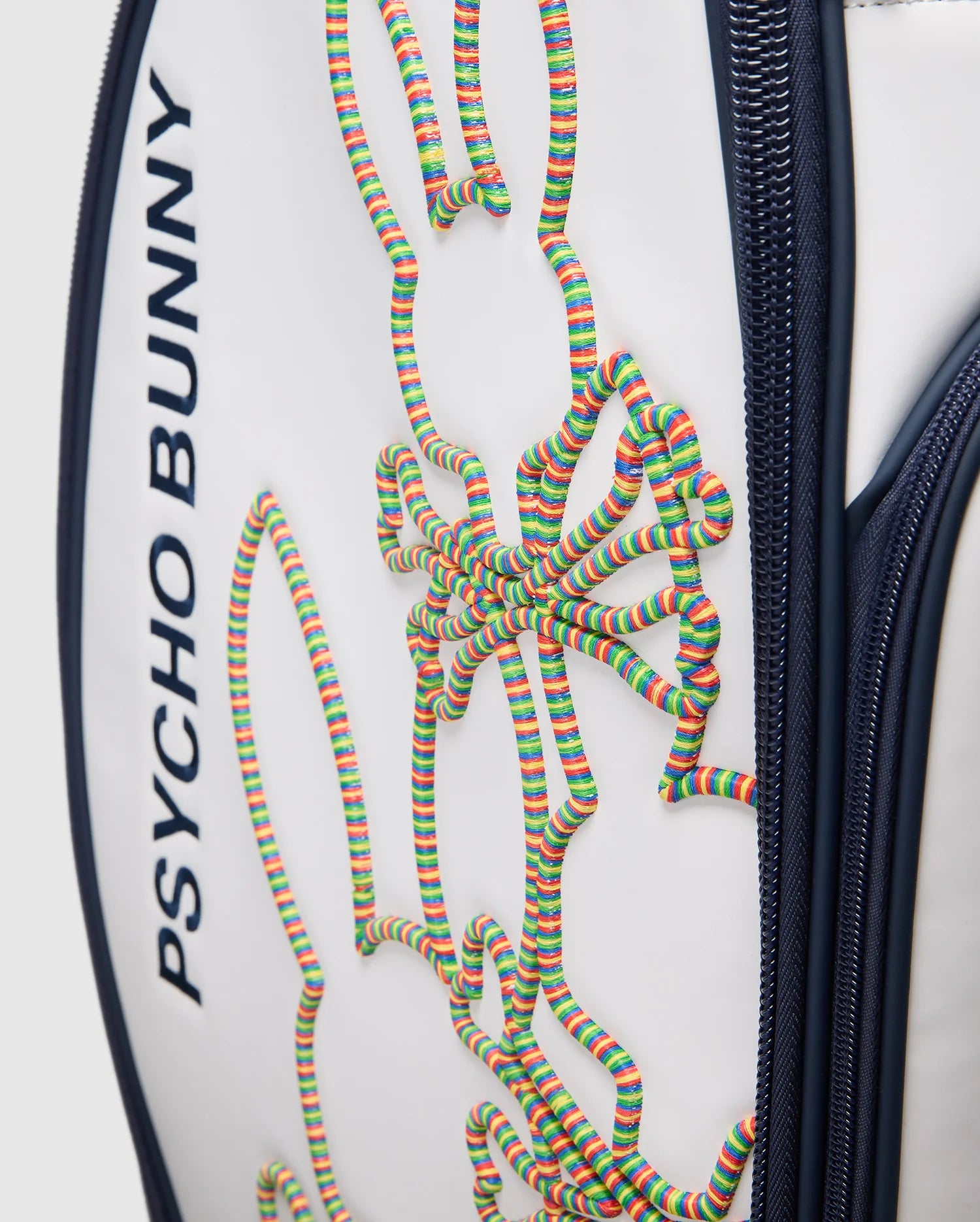 A close-up of the OUTLINE BUNNY GOLF TOUR BAG - PBMG4FC1 from Psycho Bunny shows its white polyurethane build with dark blue accents, a vibrant 3D bunny design in coiled strings, and features like zippers and five-pocket club dividers for easy organization on the course.