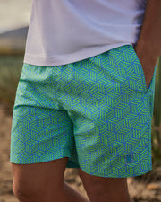 Close-up of a person wearing Psycho Bunny MENS JASPER LIGHTWEIGHT SWIM TRUNKS in brightly patterned green and blue geometric patterns, focusing on the fashion details.